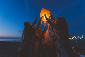 Group of friends making party on the beach at sunset time