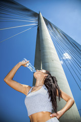 Young fit beautiful girl resting on a bridge and drinking water