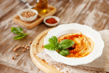 Fresh classic hummus with basil in the bowl on wooden background