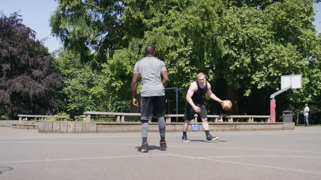 Handheld shot of two people playing basketball on an outdoor playground court