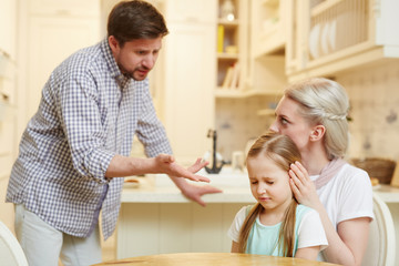 Fototapeta premium Annoyed father expressing his displeasure by little daughter while his wife reassuring the girl