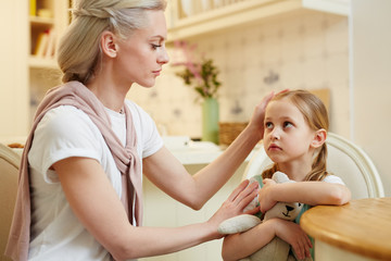 Young woman touching her little daughter head while comforting her in the kitchen