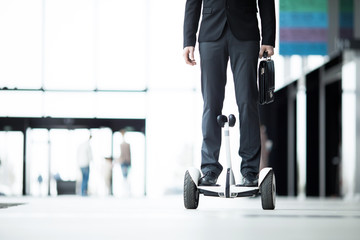 Contemporary businessman with briefcase moving on hoverboard inside business center