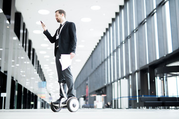 Confident young employee or security guard in suit using hoverboard for moving inside lounge