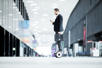 Side view of mobile and elegant businessman with briefcase messaging in smartphone while moving on...