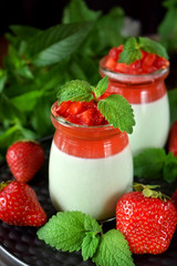 Two layered panna cotta with matcha tea topped with strawberry jelly, berries and mint in glass jars