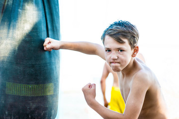 A boy with a furious and angry face waving his hand and punching a pear, looking into the camera....