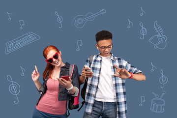 Energetic music. Happy active students feeling good and dancing while wearing earphones and listening to music