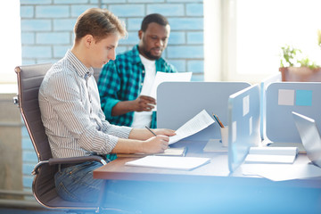 Serious young financier reading papers by individual workplace in working environment