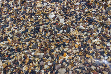 sea stones under blue water. Background of small multicolored stones lying under water.