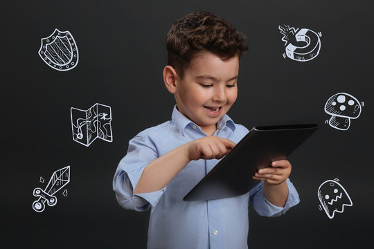 Modern kid. Modern clever little boy smiling and holding a convenient tablet while playing funny games on it