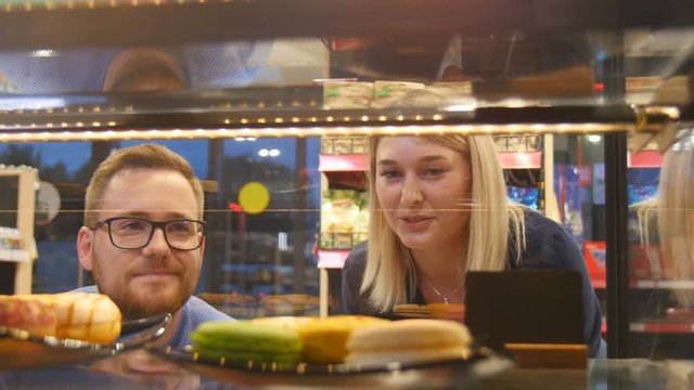 Lovers guy and girl are looking in a shop window with desserts