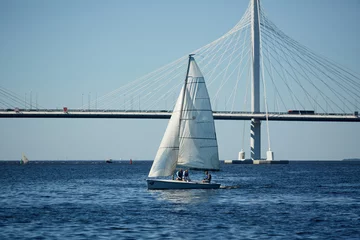 Group of humans in yacht sailing in large sea with bridge on background and blue sky above