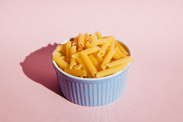 Pasta penne in blue bowl on pink background, italian cooking concept