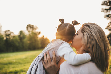 Fototapeta premium Close up portrait of beautiful woman have conversation with her child in the park. Rear view of mother telling secret to her cute girl kid. Happy family. Happy Mother's Day. Motherhood and childhood