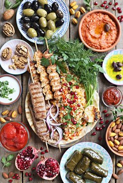 Middle eastern, arabic or mediterranean dinner table with grilled lamb kebab, chicken skewers  with roasted vegetables and appetizers variety serving on wooden outdoor table. Overhead view.