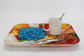 Cold, illness, treatment, autumn - a many blue capsules, pills next to a white mug with a spoon and two thermometers (digital and analog mercury) on a colored plastic tray