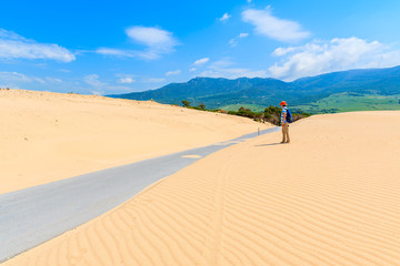 Young woman tourist backpacker standing on sand dune and looking at road to Paloma beach, Costa de la Luz, Spain