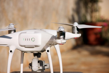 White quadcopter Drone with 4K digital camera on stand is ready for take off to fly in air to take photos, record footage from above. Drone with four motors, propellers, camera and red warning lights.