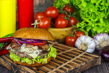 Appetizing burger on a wooden board against a background of vegetables.