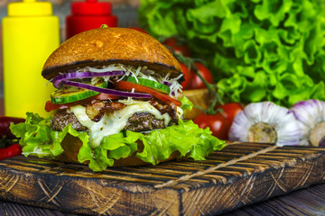 Appetizing burger on a wooden board against a background of vegetables.