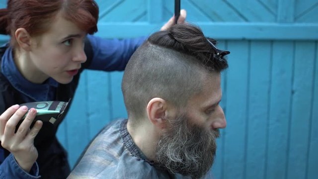 Barber woman cuts the hair of attractive middle-aged man with electric razor clipper and comb on nape