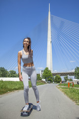 Young fit beautiful girl riding skateboard outdoor with huge bridge in the background