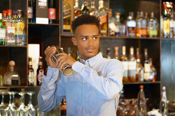  Bartender man holding in hands a shaker with a fresh delicious cocktail. Bartender shaking a cocktail shaker as she stands behind the bar mixing a drink for a client. Close-up.