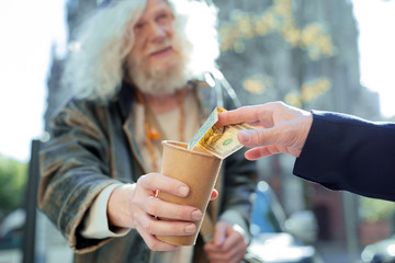 Helping homeless. Kind-hearted prosperous businessman feeling very satisfied while helping homeless...