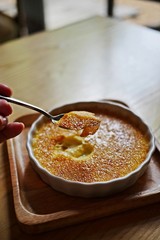 A hand of woman cracked through a crunchy top layer of a Creme brulee, burnt cream or Trinity cream, a rich and velvety custard base topped with a contrasting layer of hard caramel. Vertical.