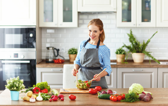 happy woman preparing vegetable salad in kitchen.