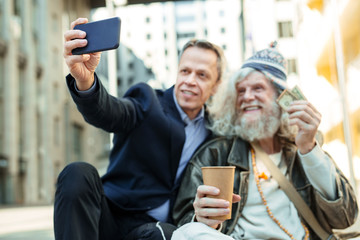 Charity man. Famous influencing charity man feeling supportive and helpful while making photo with homeless