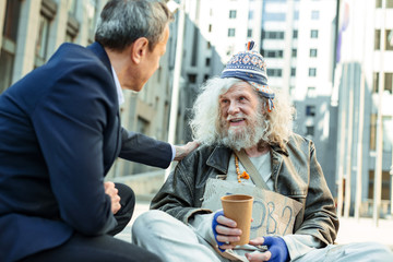 Helpful businessman. Helpful supportive businessman touching shoulder of poor refugee sitting in...