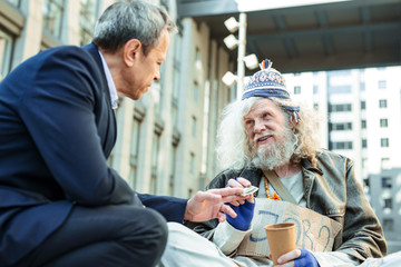 Money for food. Supportive stranger wearing black suit giving homeless man in the street some money...