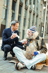 Elderly hippy. Elderly hippy man wearing bright cap receiving some food from careful kind-hearted stranger