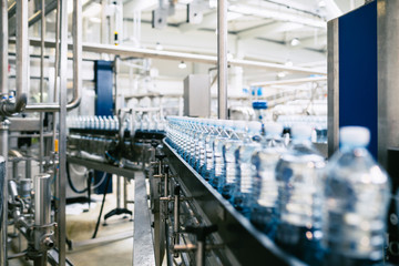 Fototapeta premium Bottling plant - Water bottling line for processing and bottling pure spring water into blue bottles. Selective focus.