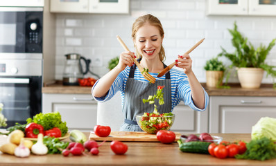 happy woman preparing vegetable salad in kitchen.
