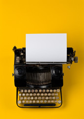 Vintage typewriter top down flatlay shot from above with empty, blank sheet of paper on yellow