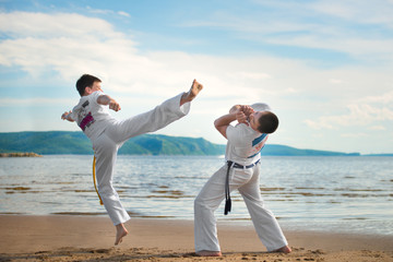 The man is a coach of capoeira and a boy practicing capoeira on the beach. Man and young guy play...