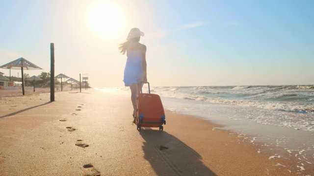 Young woman with a suitcase sitting on the beach. a young girl walks along the beach with a wheeled suitcase.Shags along the sand along the sea. The girl is looking for herself and adventure