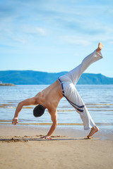 Fototapeta na wymiar Man practicing capoeira on the beach. The man does the fighting element of capoeira.