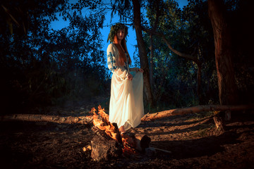 Woman in ethnic clothes with chaplet on a head near bonfire