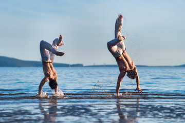 The man is a coach of capoeira and a boy practicing capoeira on the beach. Man and young guy play...
