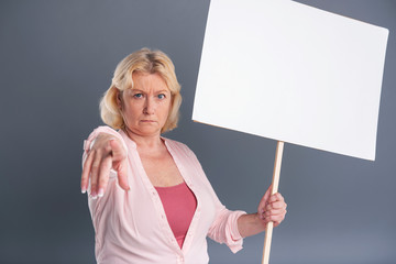 Join the protest. Fair-haired middle-aged woman holding a banner and pointing at the camera as if...