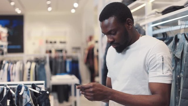 Handsome african american young man using phone texting message stand at store chooses clothes internet happy black telephone portrait cute mobile holding slow motion attractive portrait