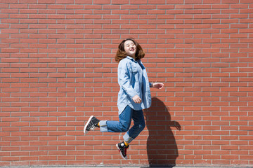 Fototapeta na wymiar Beautiful smiling young woman in a happy jump with red wall background