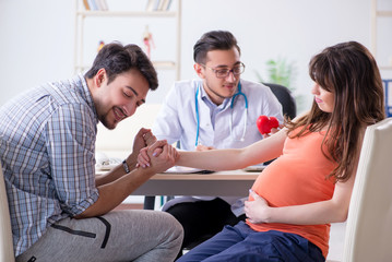 Obraz premium Pregnant woman with her husband visiting the doctor in clinic