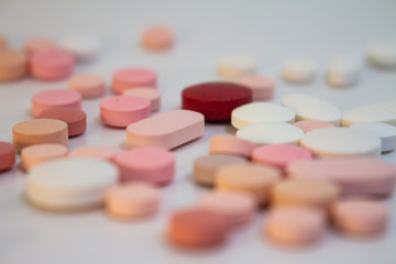 Multiple white and pink and red pills on a white background with several of them out of focus. Medications in the form of tablets.