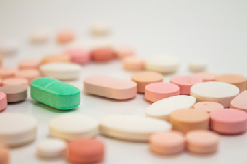 Obraz na płótnie Canvas Multiple white and pink and green pills on a white background with several of them out of focus. Medications in the form of tablets.