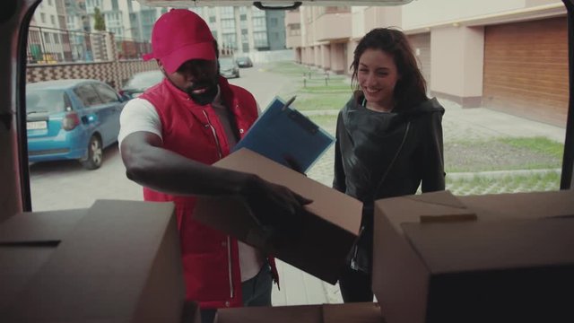 Courier African American gives a parce to a woman after signing on delivery device cardboard technology box order post postal service device sunny beard covered load logistic mailman